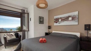 Une chambre avec un grand lit, une vue sur la mer, un canapé et un tableau au mur.