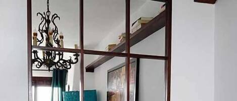 Un comedor con una mesa de madera, tres jarrones con flores rosas y un espejo grande que refleja la habitación.