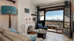 Un salon comprenant un canapé, un fauteuil et une table basse, une cheminée, et une vue sur l’extérieur par une porte vitrée.