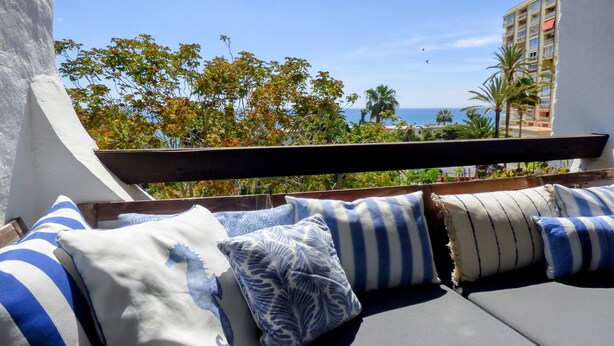 Un balcon avec vue sur la mer, comprenant un canapé agrémenté de coussins à rayures et une balustrade en bois.