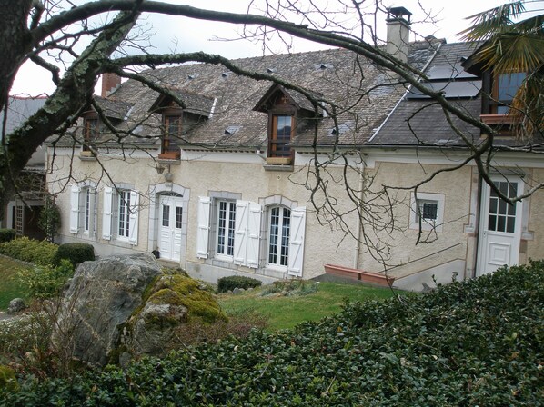 A traditional stone building with multiple windows and doors, surrounded by greenery and a large rock. - Bed and breakfast at the farm, Lourdes, Pyrenees, ANOUSTA (Loubajac)