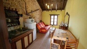 A compact kitchen with a sink, a microwave, and a small refrigerator. There is a dining table with chairs and a sofa in the living area.