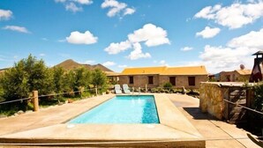 A swimming pool with a clear blue water, surrounded by a stone deck and a few lounge chairs.