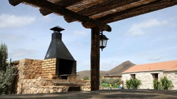 A stone building with a chimney, a wooden pergola, and a stone wall.