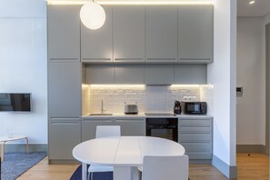 Une cuisine moderne avec des meubles gris, une table à manger blanche et un téléviseur à écran plat fixé au mur.