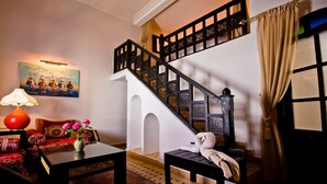 A staircase with a black railing and a white wall. There is a painting on the wall, a table with a red lamp, and a chair with a red cushion. - Room 1 - 18th century riad in the center of essaouira medina (Marrakech-Safi)