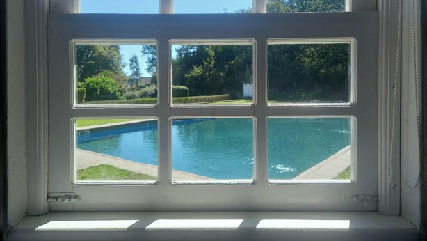 Finestra amb sis vidrieres, cadascuna amb vista a una piscina i vegetació circumdant.