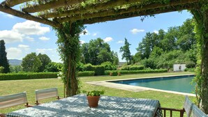 Zona de piscina amb taula i caires quadriculats, envoltada de vegetació exuberanta i un cel blau clar.