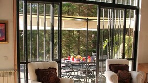 A spacious living room with two white armchairs, a coffee table, and a large sliding glass door leading to an outdoor dining area.