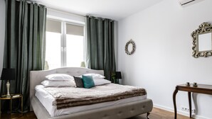 Un dormitorio ordenado con una cama grande, una mesita de noche, una pequeña mesa con tazas, un espejo y un adorno en la pared.