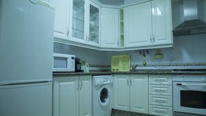 Une cuisine avec des meubles blancs, un lave-linge, un four à micro-ondes et un four traditionnel.