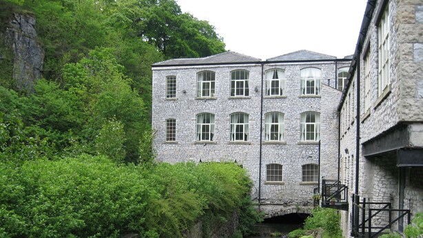 Un edificio de piedra con varias ventanas y un puente sobre un arroyo.