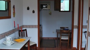 Un coin repas avec une table, des chaises, un luminaire suspendu jaune et une cuisine en arrière-plan.