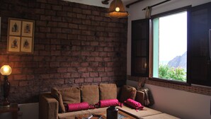 Une pièce chaleureuse avec un mur en briques, un plafond en bois, un canapé avec des coussins, une table avec un vase et une fenêtre donnant sur un paysage verdoyant.