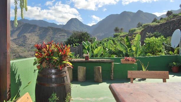 Une terrasse avec un banc en bois, un pot de fleurs et une vue sur les montagnes.