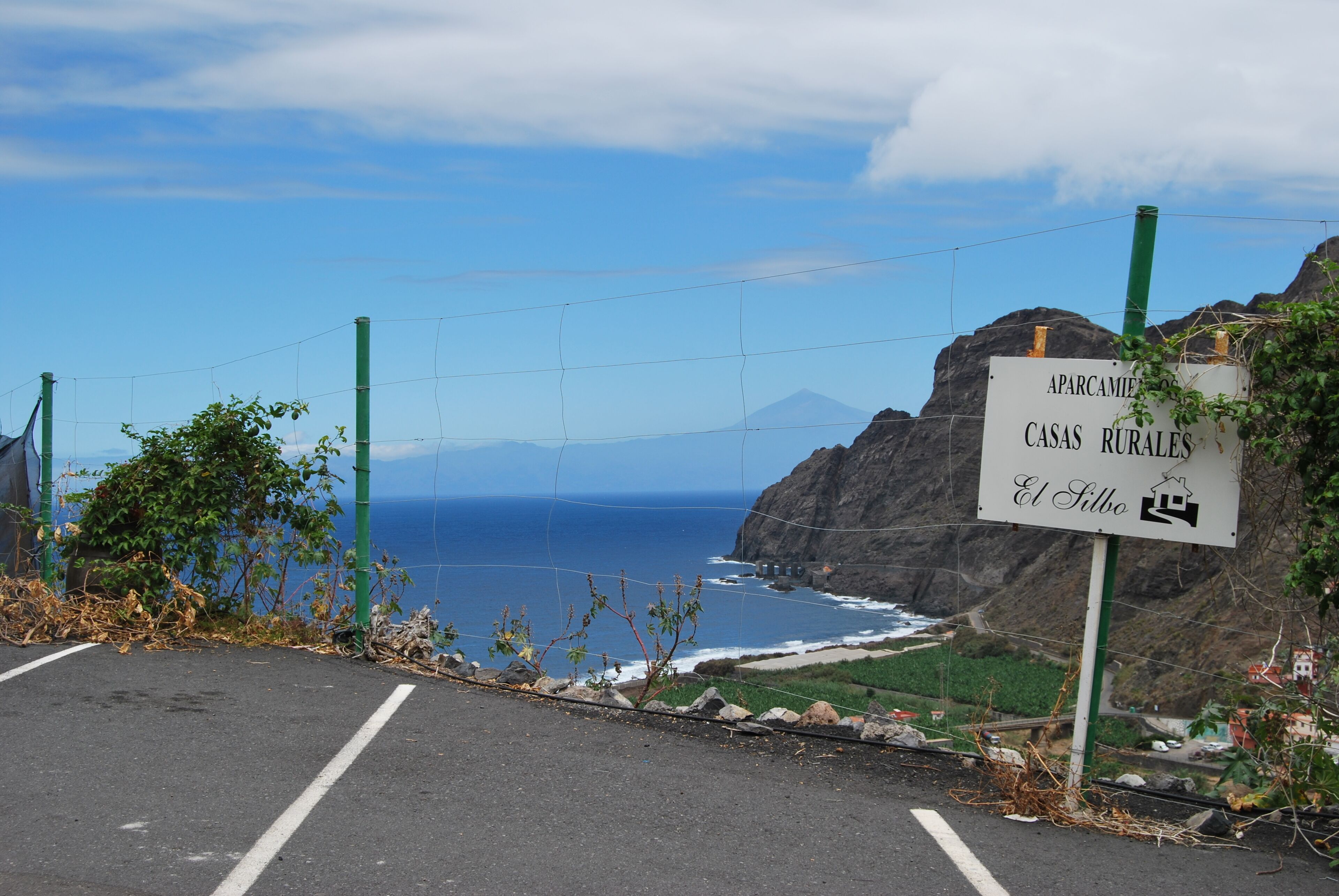 Une route côtière avec un panneau indiquant « APARCAMENTOS CASAS RURALES El Silbo ».