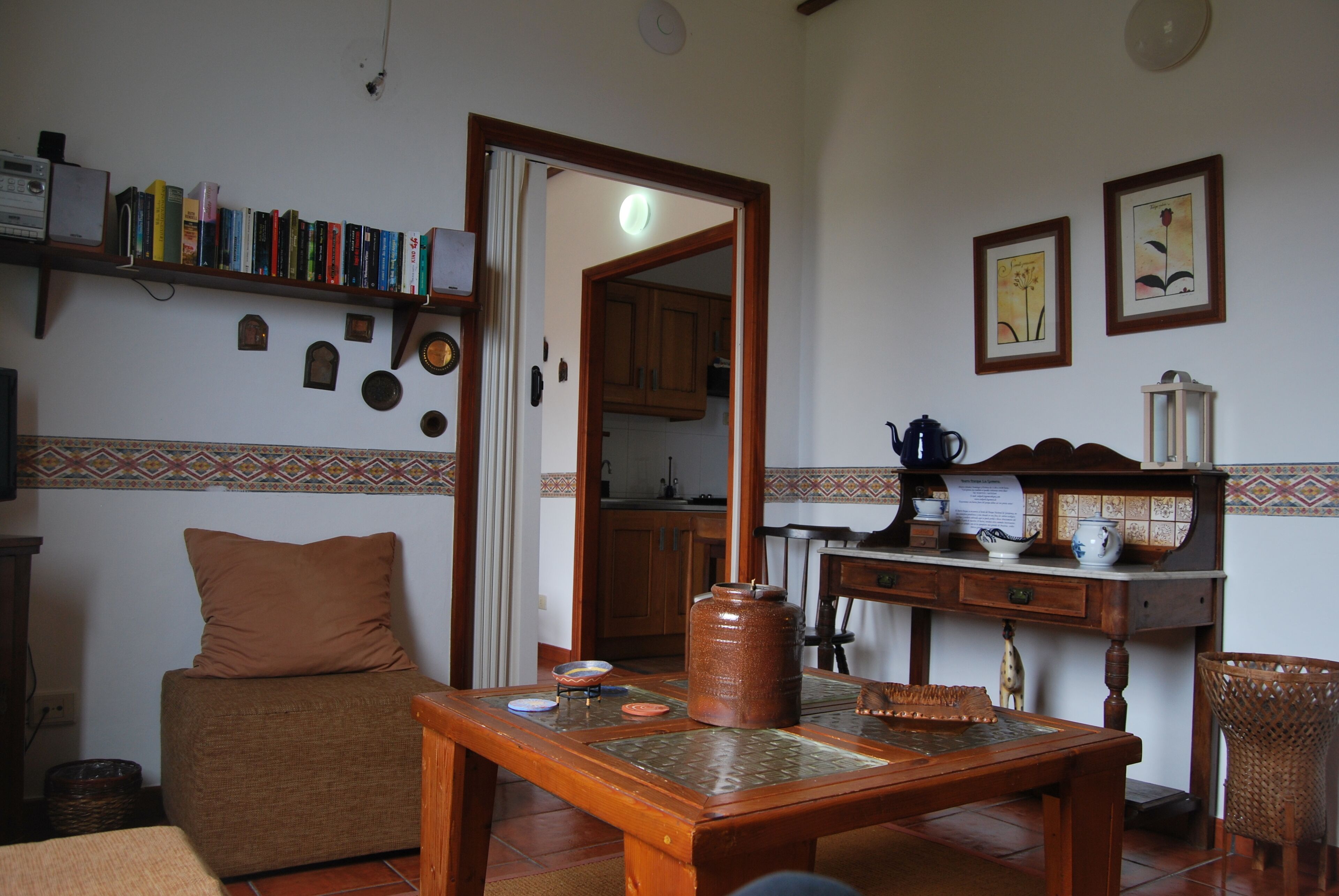 Un salón acogedor con un sofá, una mesa de centro, una estantería y una cocina visible a través de un vano abierto.