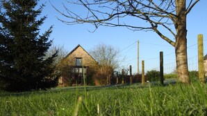 Una casa in pietra con un'ampia finestra e una porta, immersa in un prato erboso e alberi.