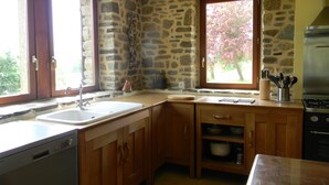 Cucina con pareti in pietra, mobili in legno, lavello in acciaio inossidabile e piano cottura a gas.