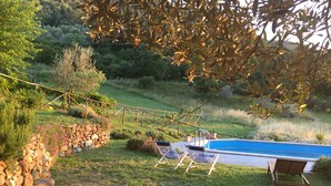 Una piscina con sillas de descanso, un muro de piedra y una zona verde con árboles.