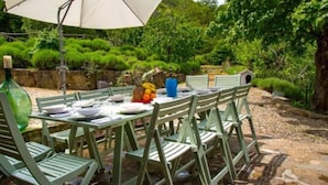 Un área de comedor al aire libre con una mesa lista para cuatro personas, rodeada de sillas verdes.