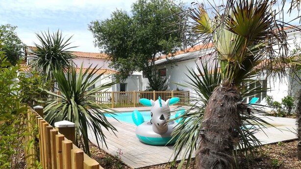 A pool area with a wooden fence, inflatable pool toys, and tropical plants. - House 4 people near sea (Les Sables-d'Olonne)