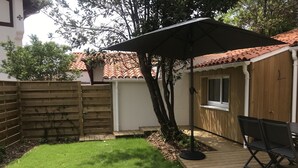 A wooden deck with a table and chairs, a covered patio area, and a fenced backyard. - House 4 people near sea (Les Sables-d'Olonne)