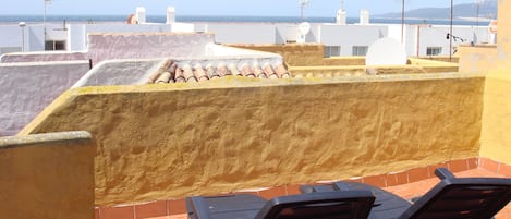A rooftop terrace with two lounge chairs, a view of the sea, and satellite dishes.