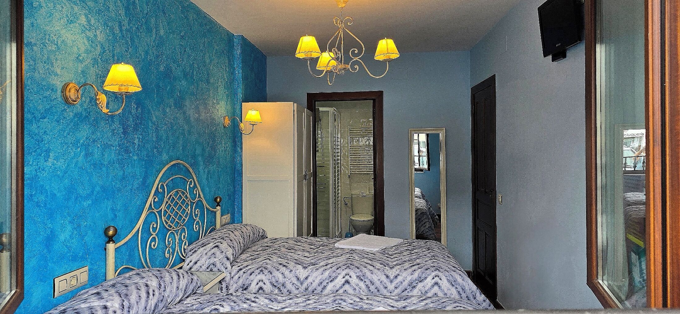 A bedroom with a bed, a chandelier, and a mirror.