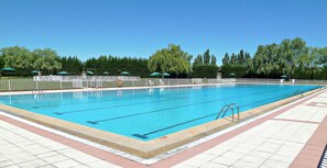 Ein Schwimmbecken mit Fliesen umgeben von Bäumen und Sonnenschirmen.