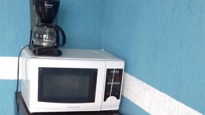 Ein schwarzer Kühlschrank mit einer Mikrowelle darauf, einer Kaffeemaschine und einem gelben Warnhinweis.