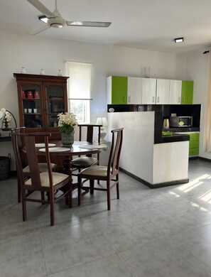 A dining area with a round table and chairs, a cabinet with glass doors, and a kitchen area with green and white cabinets. - fully furniture cinnamon apartment with privet roof garden (Panadura)
