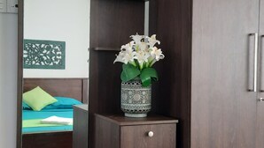 Un dormitorio con cama, armario, espejo y un jarrón decorativo con flores.
