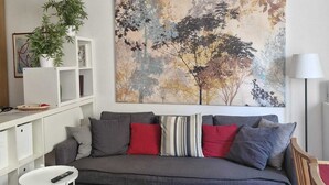 A modern living room with a grey sofa, a large abstract painting, a white shelving unit, and a small white table. - In Florence, sunny and beautiful two-story flat, well connected to the center (Firenze)