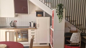 A compact kitchen with white cabinets, a dining table with a red tablecloth, a staircase with a metal railing, and a living area with a sofa and a patterned rug. - In Florence, sunny and beautiful two-story flat, well connected to the center (Firenze)