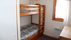 Una cama litera con ropa de cama estampada, una escalera de madera, una mesita pequeña y una ventana con cortinas.