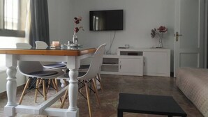 Une pièce moderne et bien éclairée, comprenant une table à manger, des chaises, un téléviseur et un lit.