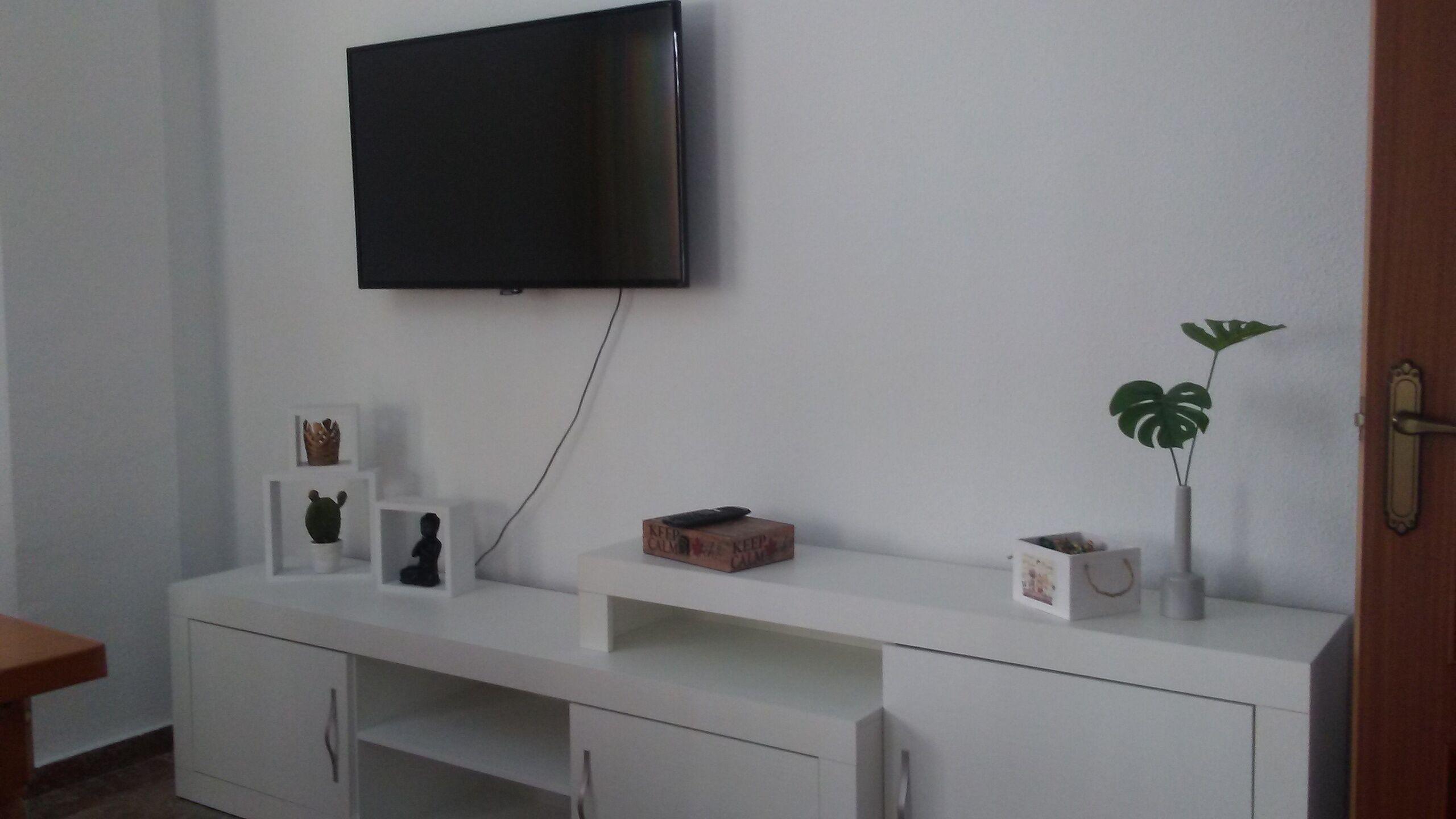 Un mueble blanco de entretenimiento con un televisor de pantalla plana montado encima, una planta pequeña y algunos objetos decorativos.
