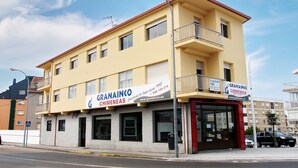A two-story building with a yellow facade and a red roof. The ground floor has a large glass window and a sign for GRANAINCO CHIMNEAS. There is a balcony on the second floor.