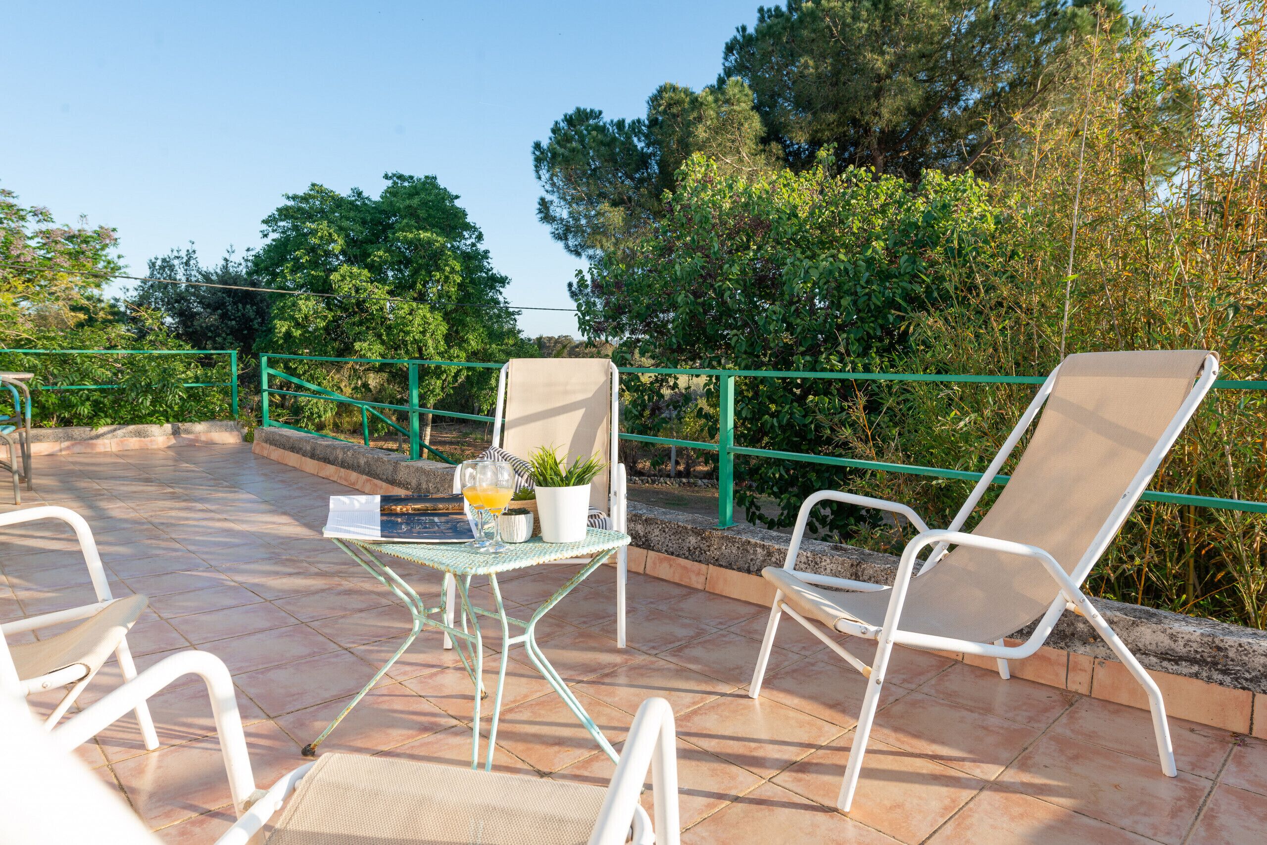 A terrace with two white lounge chairs, a glass table with a potted plant, and a drink.