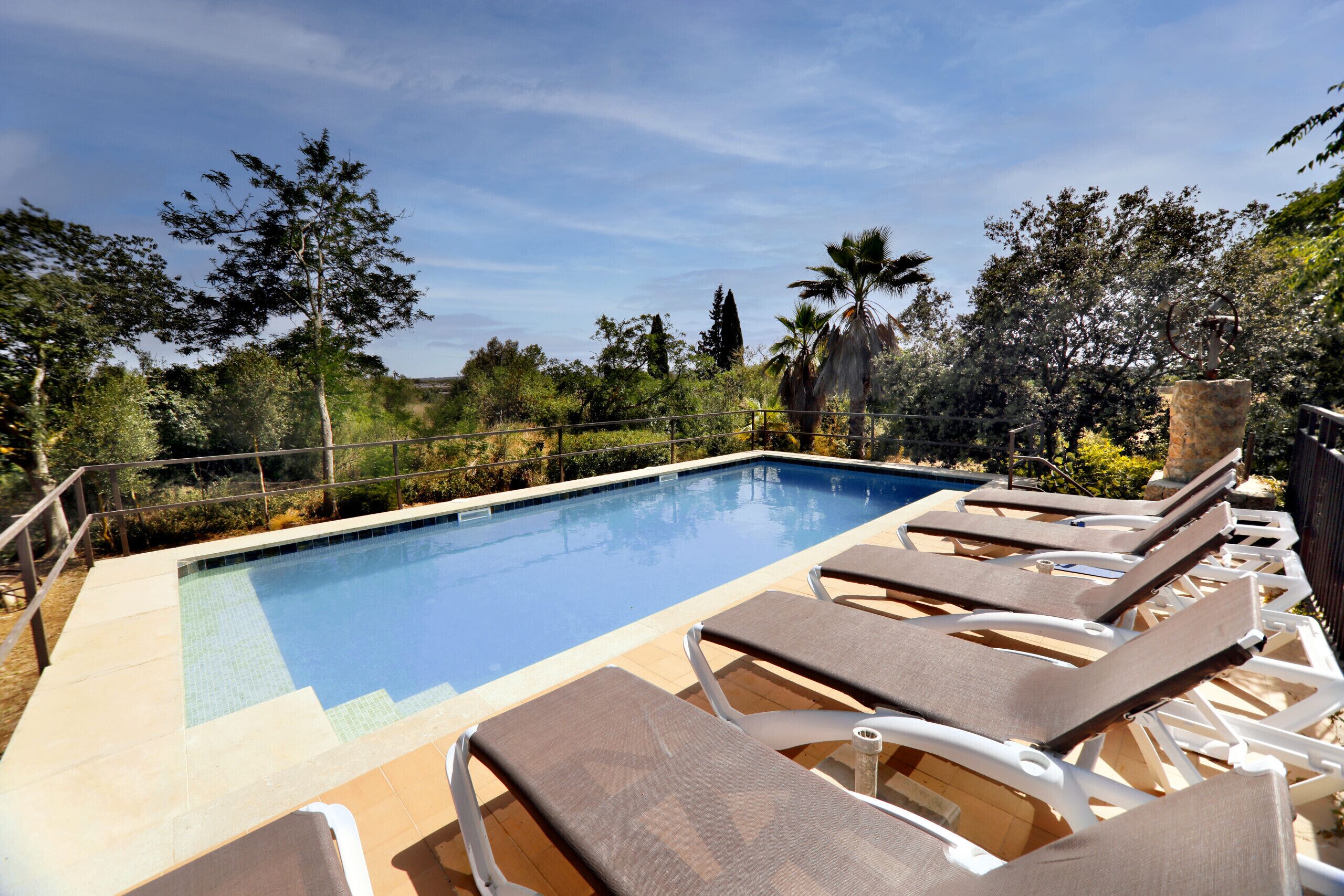 A pool area with lounge chairs and a clear blue pool surrounded by greenery.
