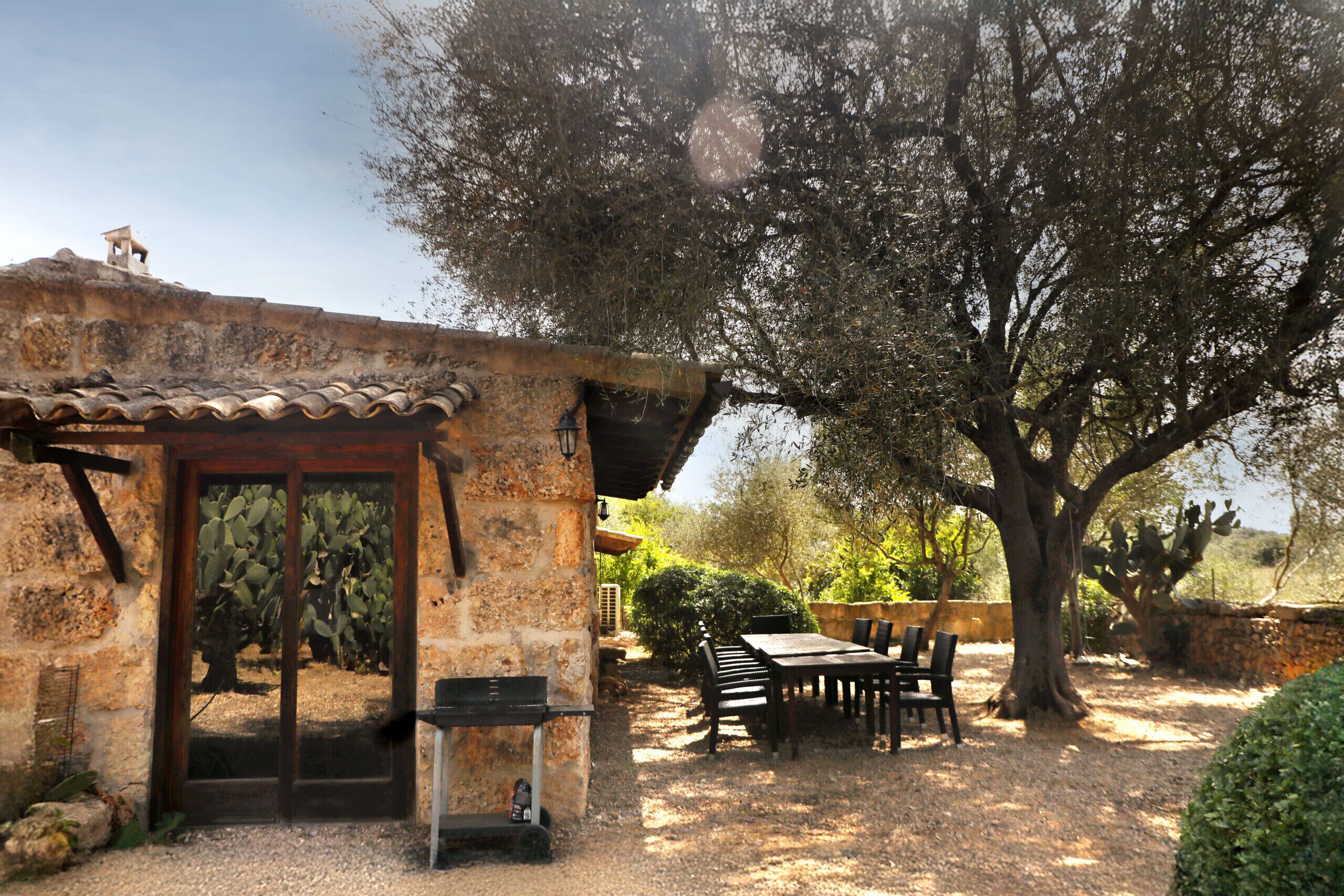 A rustic stone building with a tiled roof, a wooden door, and a patio area with a table and chairs.
