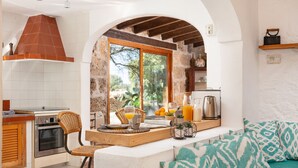 A kitchen with a stone wall, wooden beams, a large window, and a breakfast setup. - Sunset Ecofinca Can Vey - Country house with private pool (Inca)