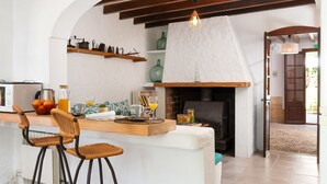 A kitchen with a wooden island, bar stools, a fireplace, and shelves with decorative items. - Sunset Ecofinca Can Vey - Country house with private pool (Inca)