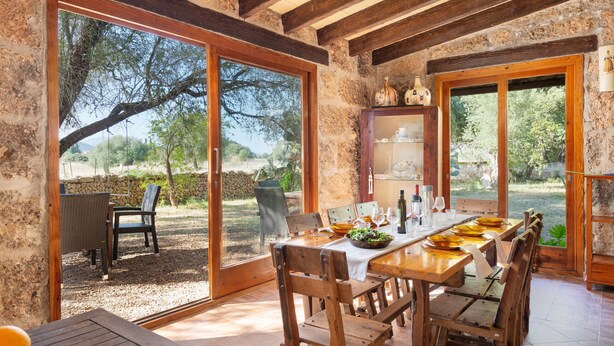 A rustic dining area with a wooden table and chairs, large windows, and a view of the outdoors. - Sunset Ecofinca Can Vey - Country house with private pool (Inca)