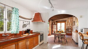 A kitchen with a large island, wooden cabinets, a stove, and a dining area with a table and chairs. - Sunset Ecofinca Can Vey - Country house with private pool (Inca)
