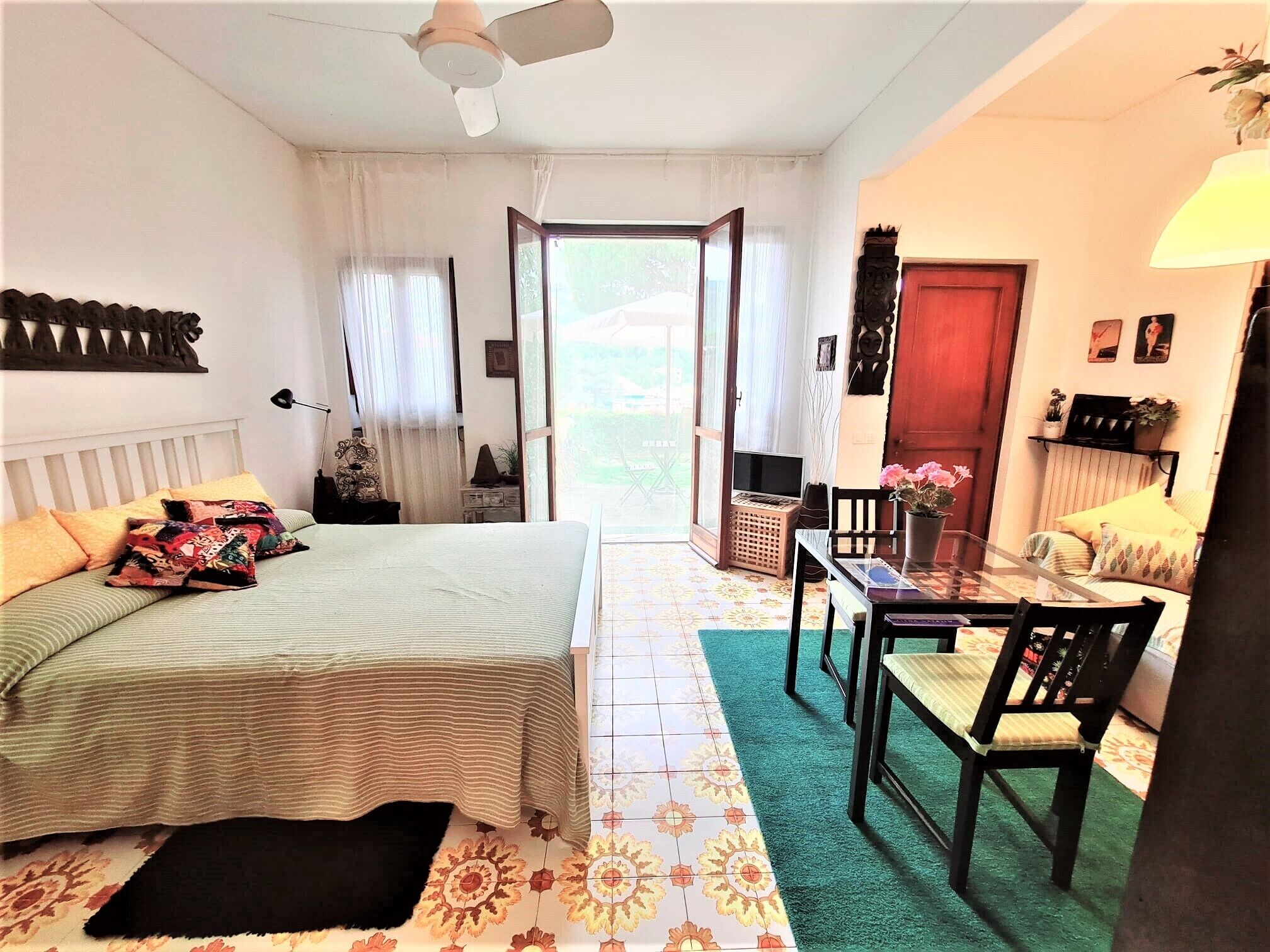 Ein Schlafzimmer mit einem Bett, einem Schreibtisch und einem Stuhl. Es gibt ein Fenster, eine Tür und einen Deckenventilator.