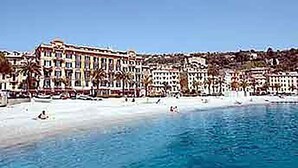 Un hotel frente al mar, de varios pisos, con una playa en primer plano y un cielo azul despejado.
