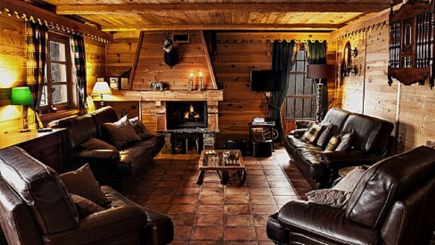 A cozy log cabin interior with leather sofas, a fireplace, and wooden walls.