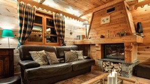A cozy cabin interior with a leather sofa, a wooden coffee table with candles, and a fireplace.